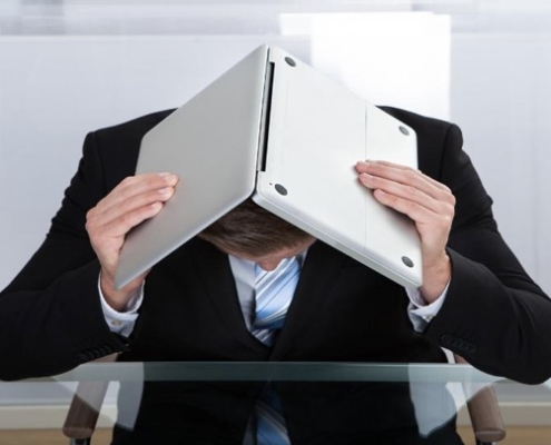 A man holding an open laptop computer over his face.