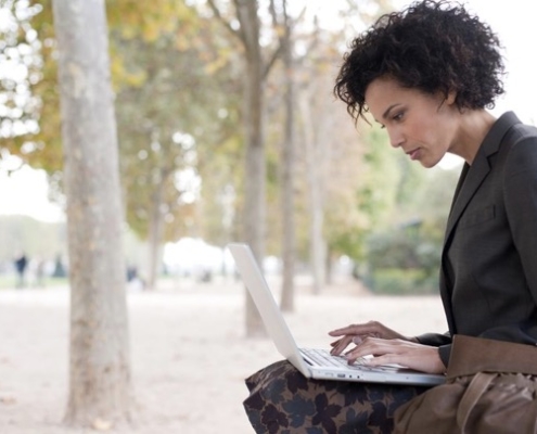 A woman is using her laptop outside on the street.