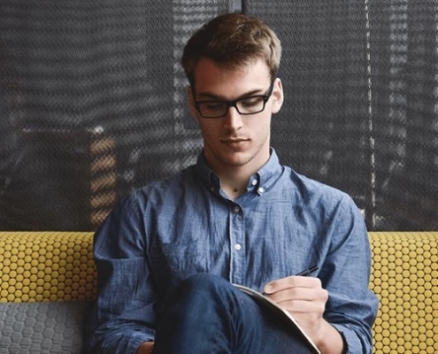 A man sitting on top of a couch writing.